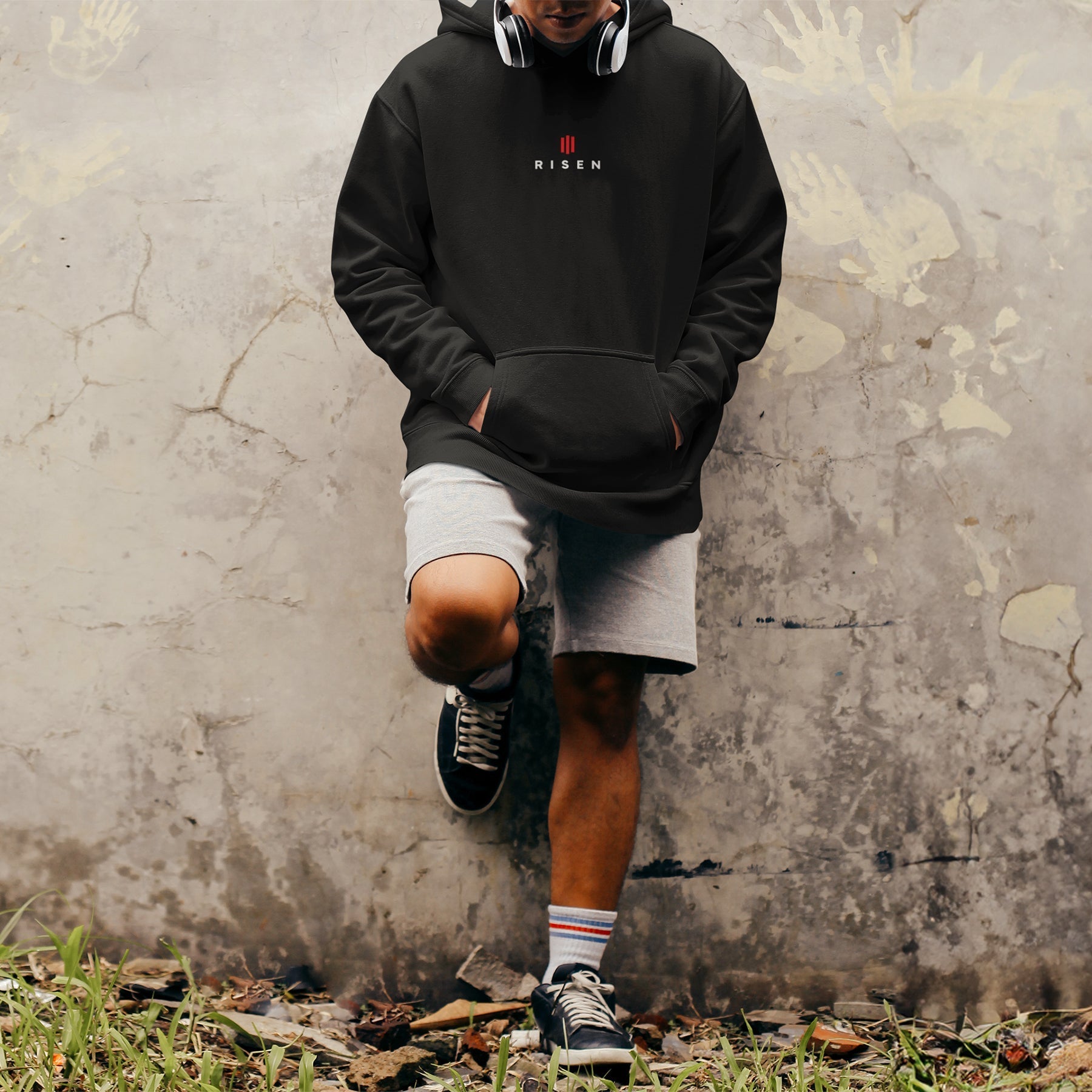Image of A man standing against the wall wearing a black Risen hoodie.