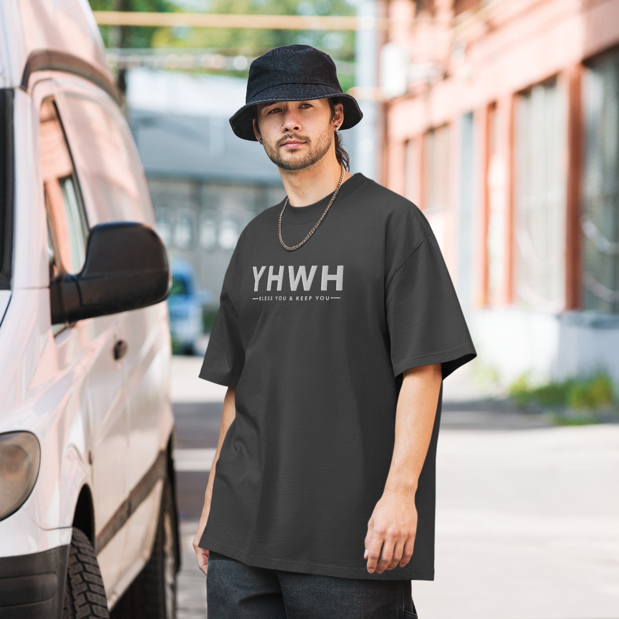 A man next to a van with a hat and a grey oversized t-shirt that reads 