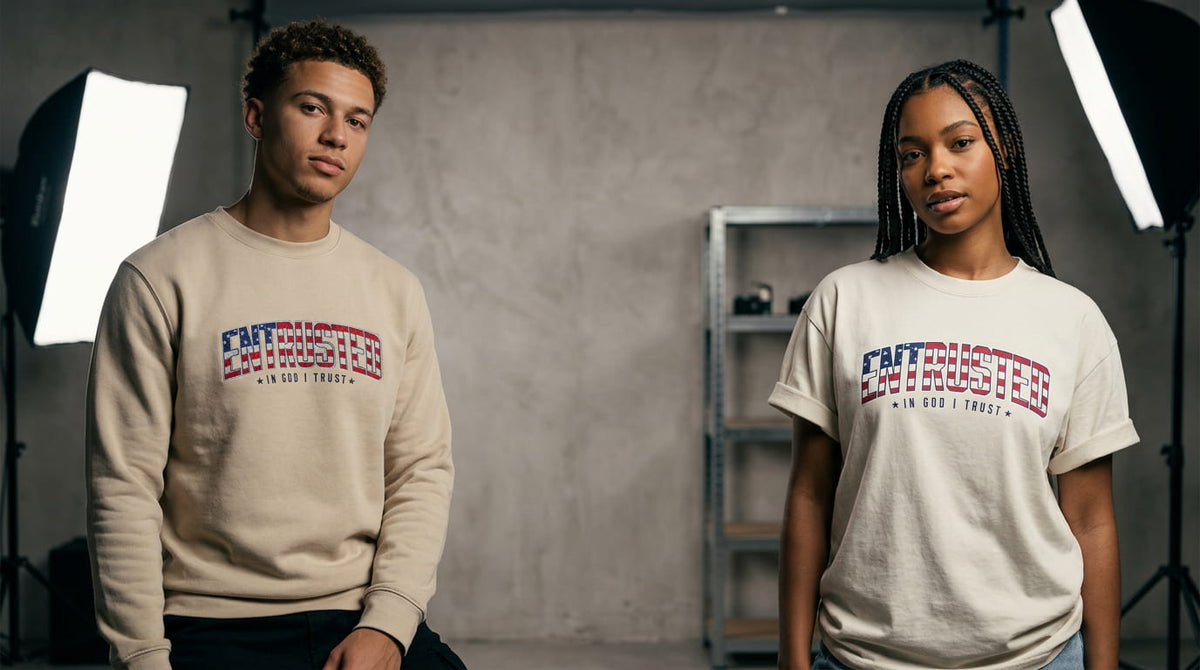 Two models wearing the Entrusted Patriotic Edition sweatshirt and oversized tee with the American flag ENTRUSTED In God I Trust design in a photo studio