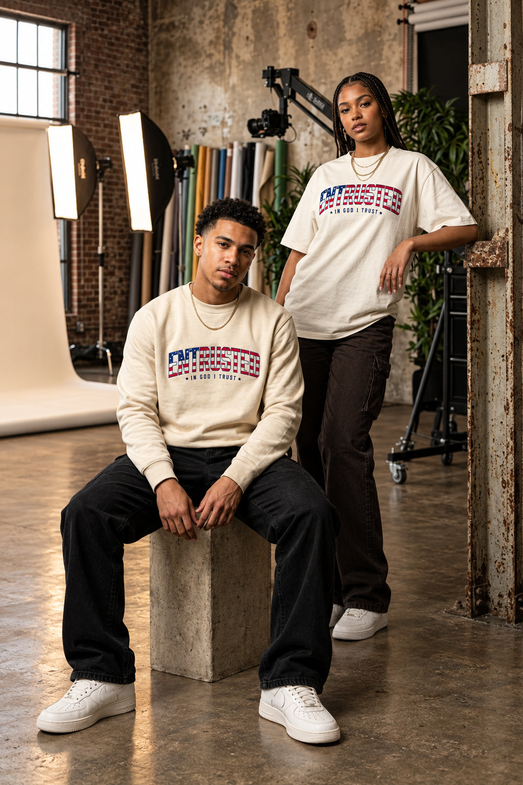 A man and a woman wearing the Entrusted Patriotic Edition sweatshirt and oversized tee with the American flag ENTRUSTED In God I Trust design