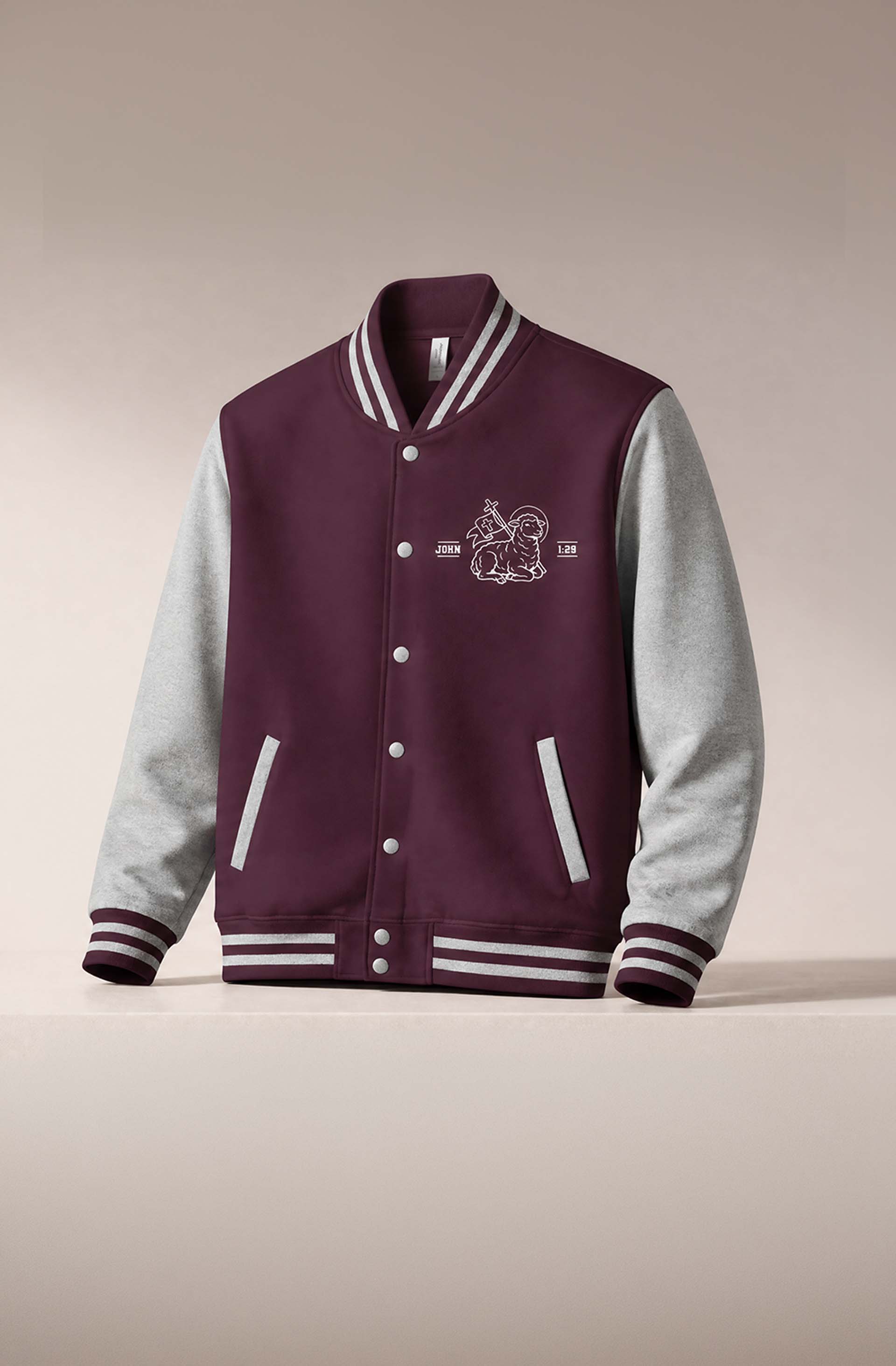 Maroon and grey varsity letterman jacket embroidered with a lamb and cross graphic and a "John 1:29" scripture reference, mobile crop.