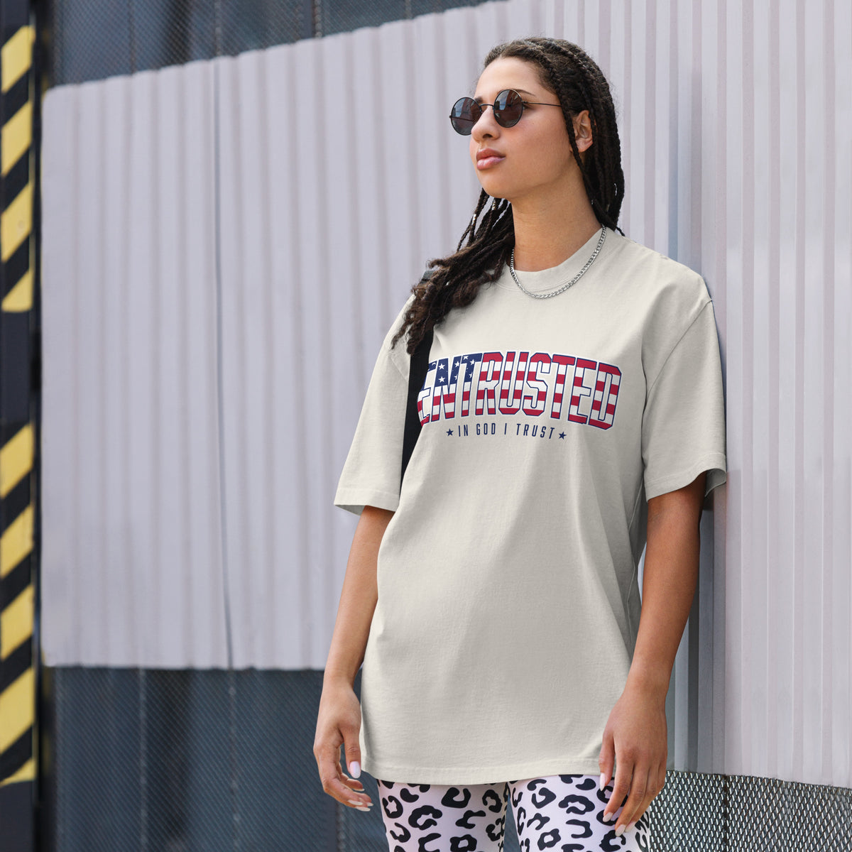 Woman wearing the Entrusted patriotic oversized faded tee in Faded Bone with the flag-pattern ENTRUSTED design