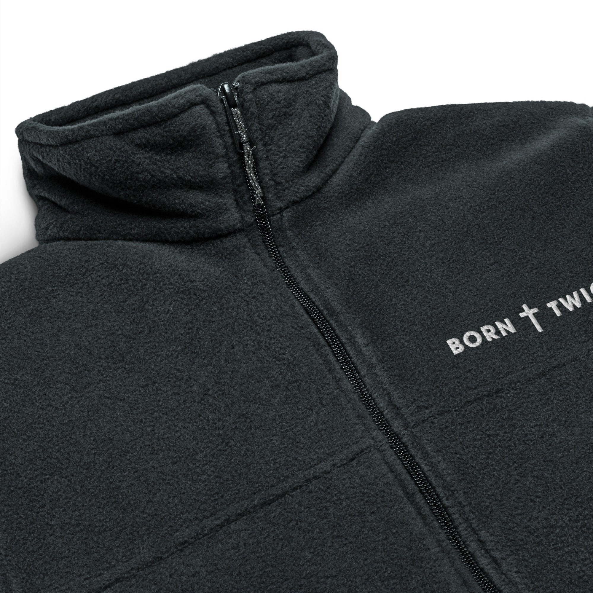 Image of Close-up of the embroidered BORN TWICE cross wordmark, zipper and fleece collar on the black Columbia jacket