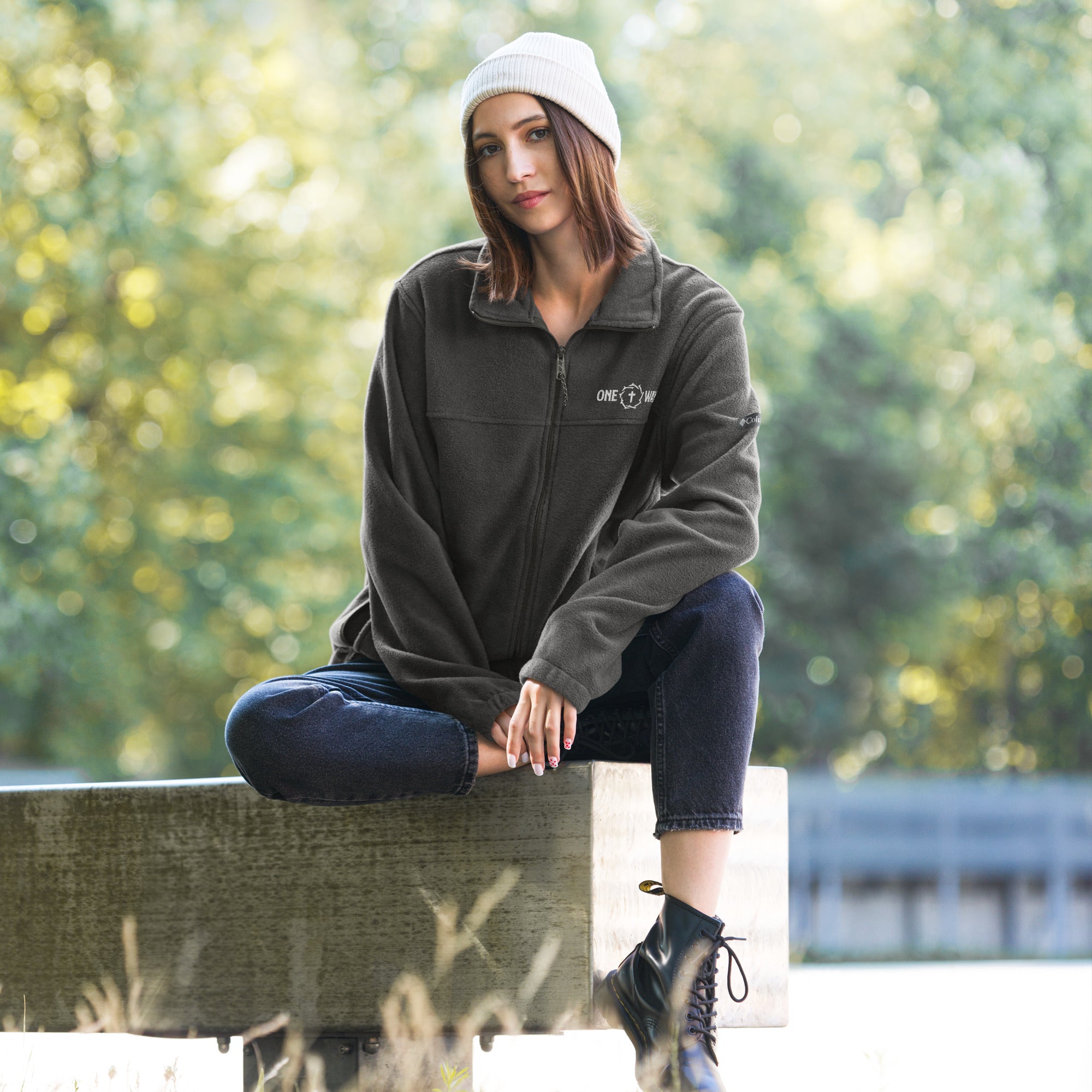 Image of Woman sitting outdoors in the One Way Columbia fleece jacket in charcoal heather with a white beanie